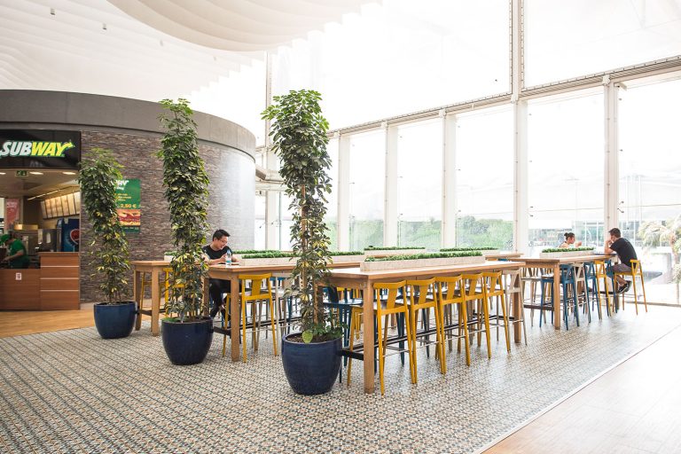Food court com mesas, cadeiras e plantas